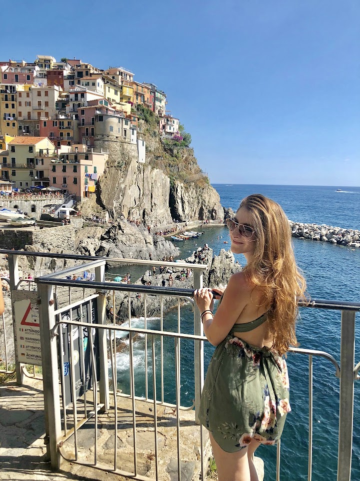 Picture of Julia in front of the colorful houses on a hill in Manarola, Cinque Terre, taking a day trip from Florence.